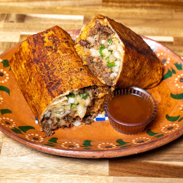 Two halves of a large, grilled burrito filled with meat, rice, and onions, served with dipping sauce.
