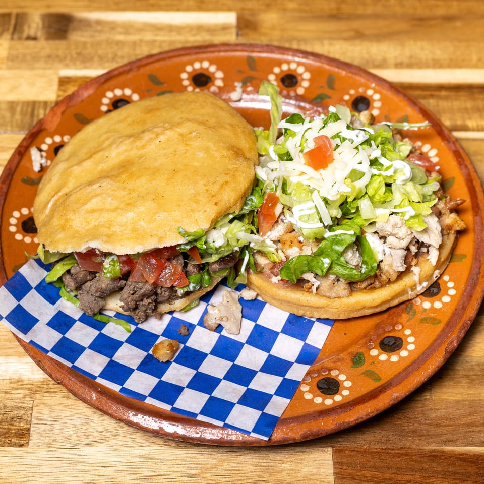 Two sopes, one with beef and the other with chicken, topped with lettuce, tomato, and cheese.