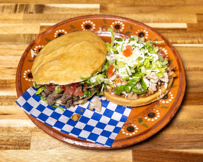 Two sopes, one with beef and the other with chicken, topped with lettuce, tomato, and cheese.