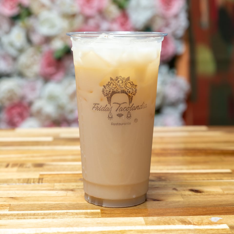 A plastic cup of iced horchata with the Frida's Tacolandia logo sits on a wooden table.