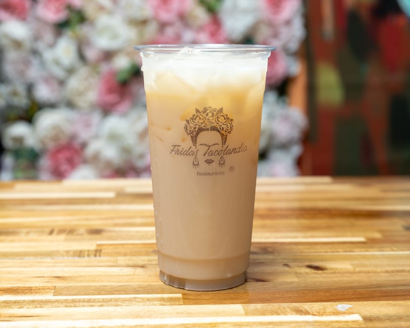 A plastic cup of iced horchata with the Frida's Tacolandia logo sits on a wooden table.