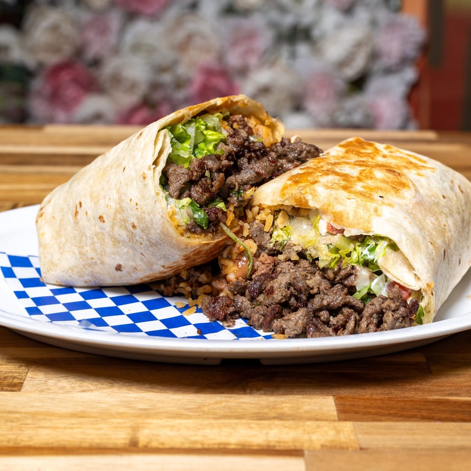 A large burrito, cut in half, revealing seasoned meat, rice, and lettuce on a white plate.