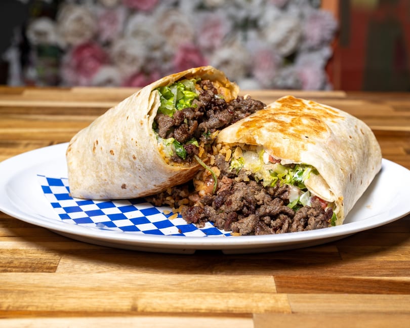 A large burrito, cut in half, revealing seasoned meat, rice, and lettuce on a white plate.