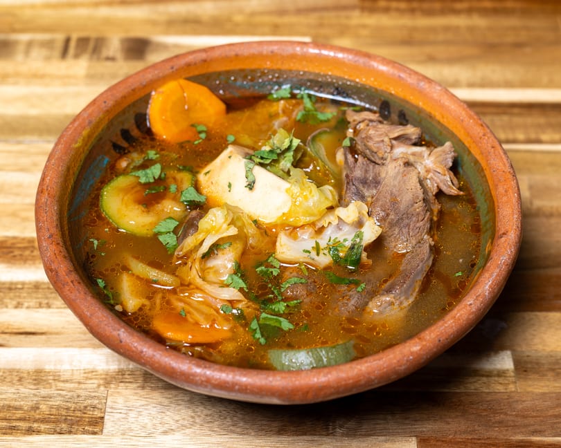 Hearty beef and vegetable soup with carrots, zucchini, cabbage, and cilantro in a rustic bowl.