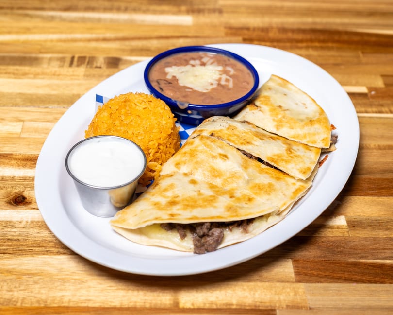 A white plate with beef quesadillas, rice, refried beans, and a side of sour cream.