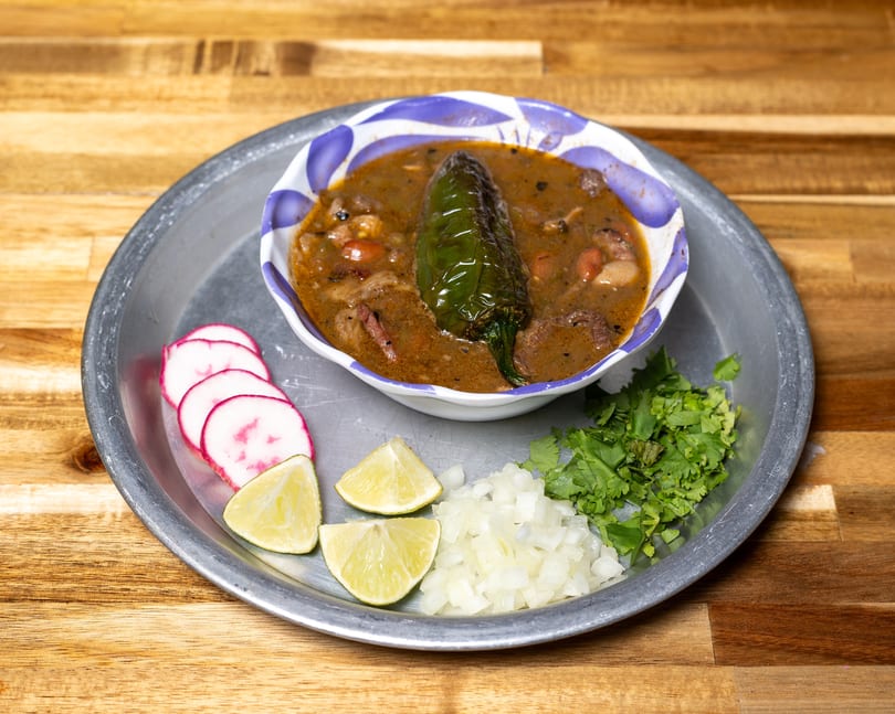 Hearty bean and meat soup with a green chili, served with radishes, lime, onion, and cilantro.