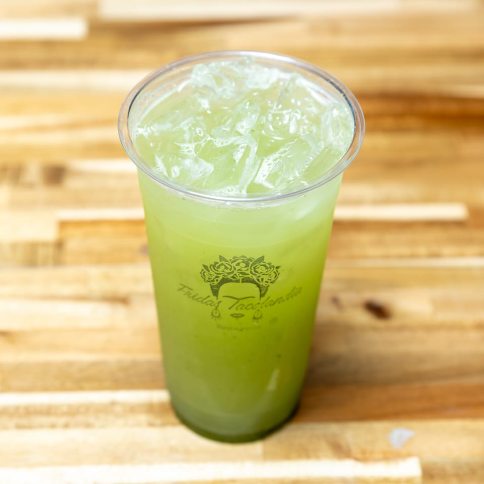 A plastic cup of green iced horchata from Fridas Tacolandia sits on a wooden table.