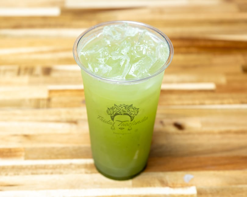 A plastic cup of green iced horchata from Fridas Tacolandia sits on a wooden table.