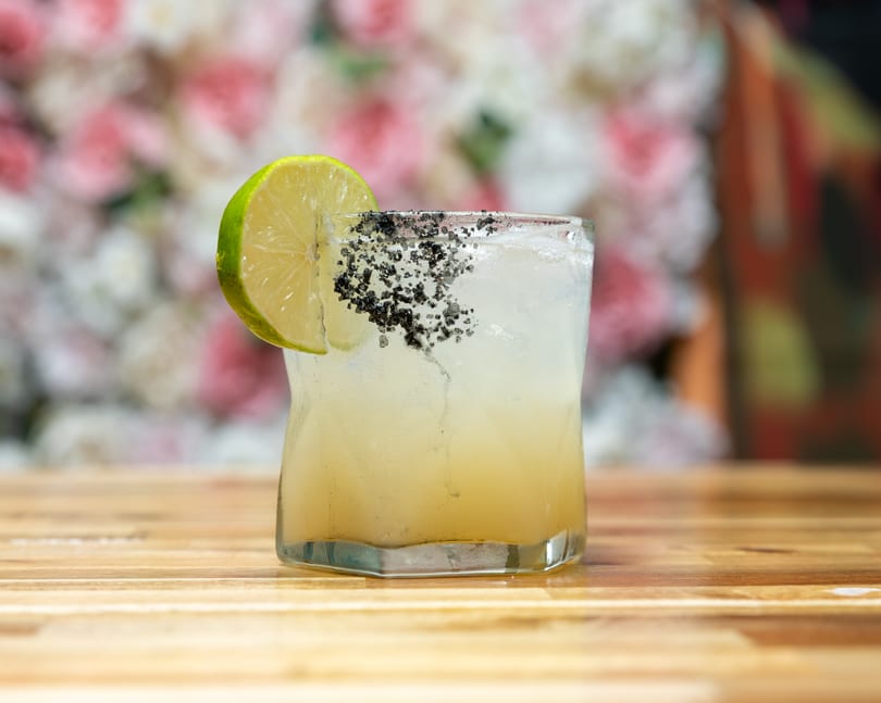 A margarita with a black salt rim and lime wedge sits on a wooden table.