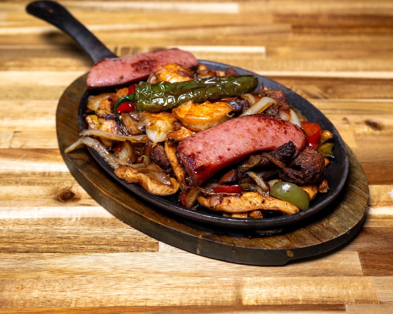 Sizzling fajitas with sausage, shrimp, chicken, peppers, and onions in a cast iron skillet.