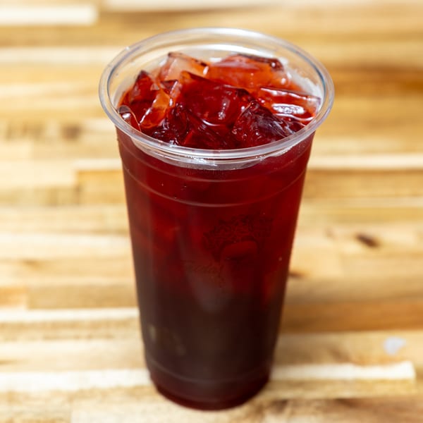 A plastic cup filled with a dark red iced drink, possibly hibiscus tea, on a wooden surface.