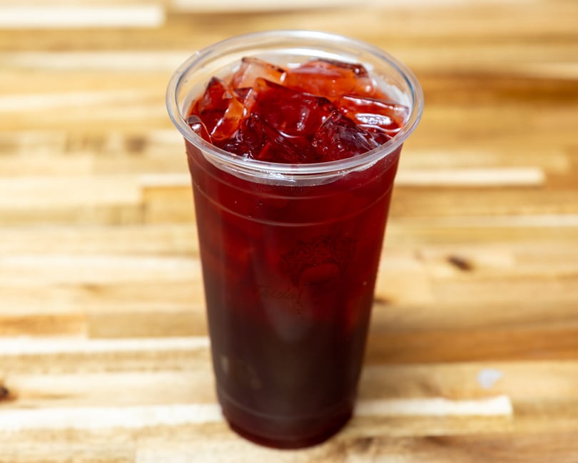 A plastic cup filled with a dark red iced drink, possibly hibiscus tea, on a wooden surface.
