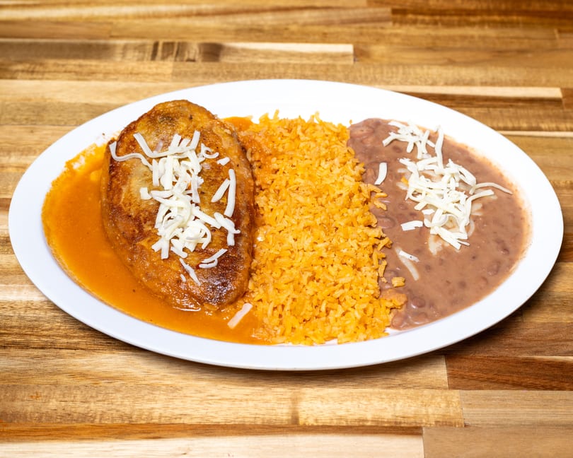 Chili relleno covered in sauce and cheese, with a side of rice and refried beans.