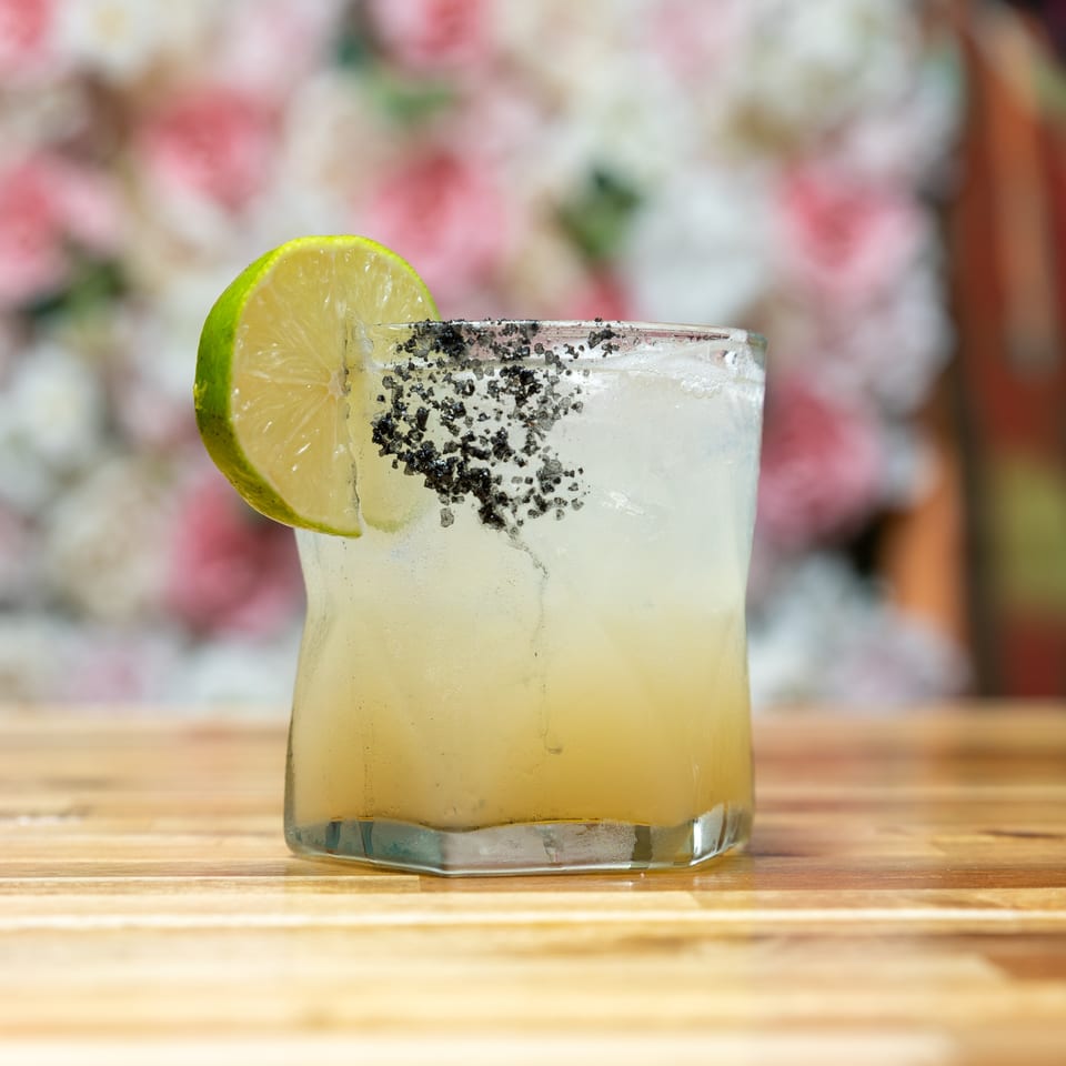 A refreshing cocktail with a lime wedge and black salt rim sits on a wooden table.