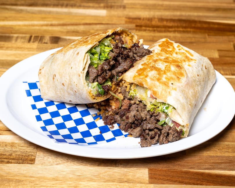 A large beef burrito, cut in half, revealing meat, rice, and lettuce on a white plate.