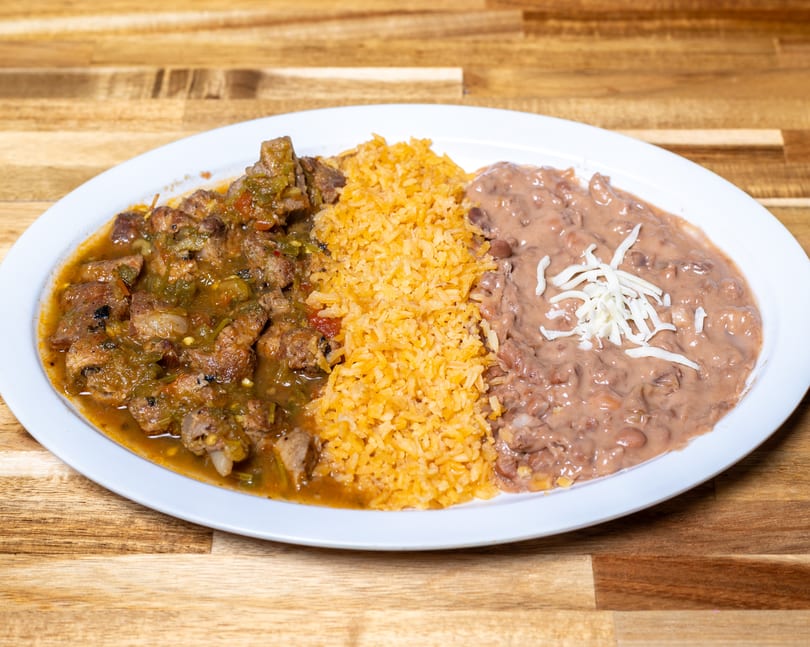 Pork chile verde, orange rice, and refried beans with shredded cheese on a white plate.