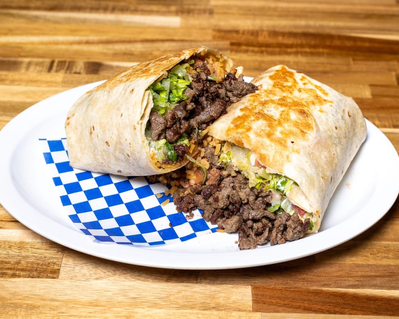 A large beef burrito, cut in half, revealing meat, rice, and lettuce on a white plate.