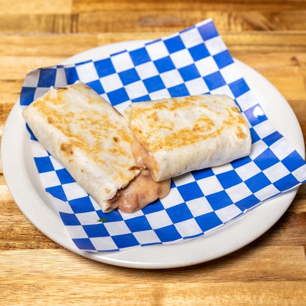 Two golden-brown burritos with melted cheese and beans spilling out, on blue and white checkered paper.