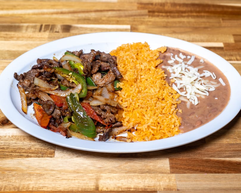 Beef fajitas with bell peppers and onions, served with rice and refried beans topped with cheese.