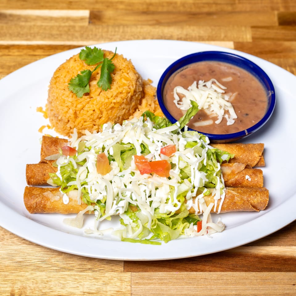A plate of Mexican food with taquitos, rice, and refried beans on a wooden table.
