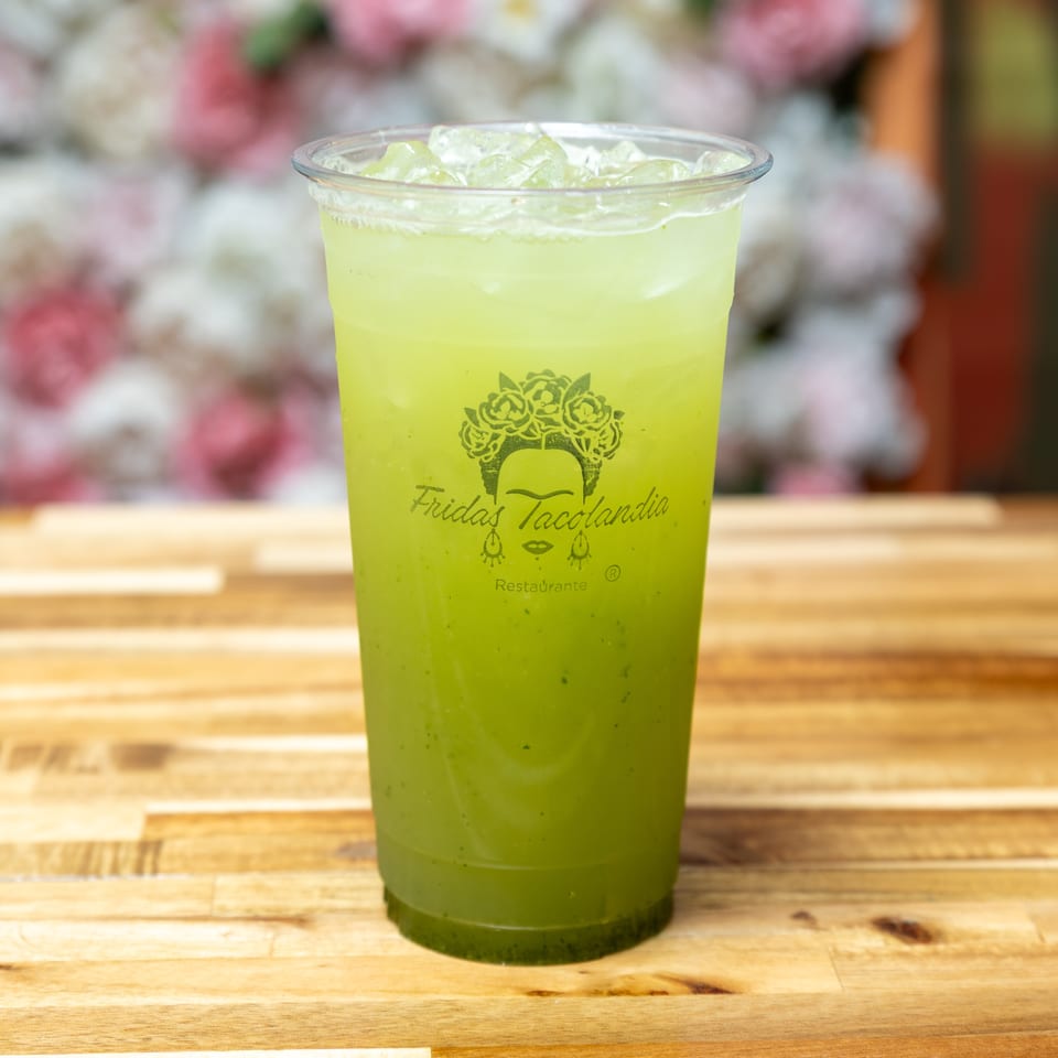 A Fridas Tacolandia branded cup of green iced drink sits on a wooden table.