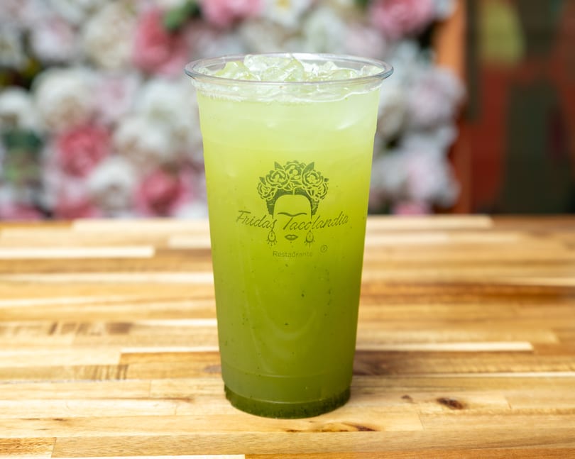 A Fridas Tacolandia branded cup of green iced drink sits on a wooden table.